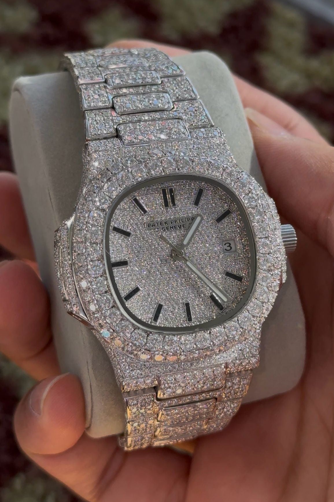 Silver watch with gemstone accents held in a hand against a blurred background